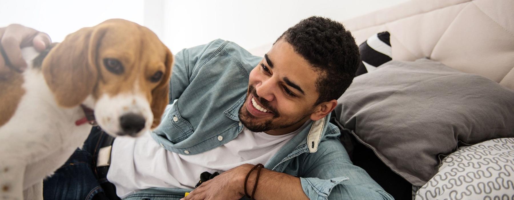 man smiles and pets his dog on a bed