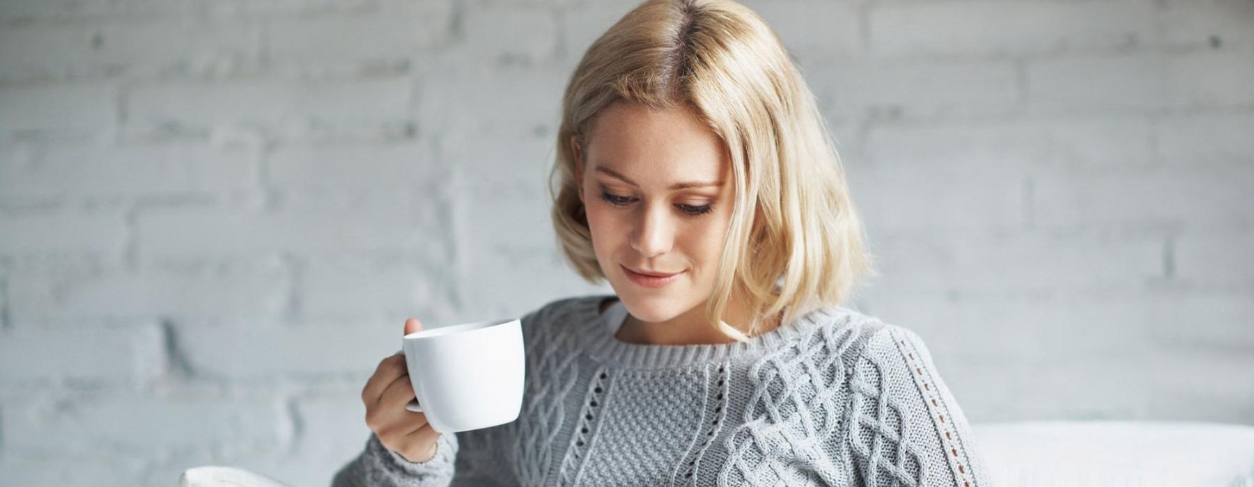 a woman sits on a couch with a cup of coffee and looks at her tablet